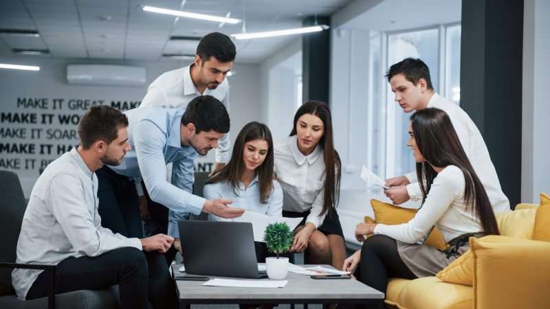 Guy shows document to a girl. Group of young freelancers in the office have conversation and working Vacantes